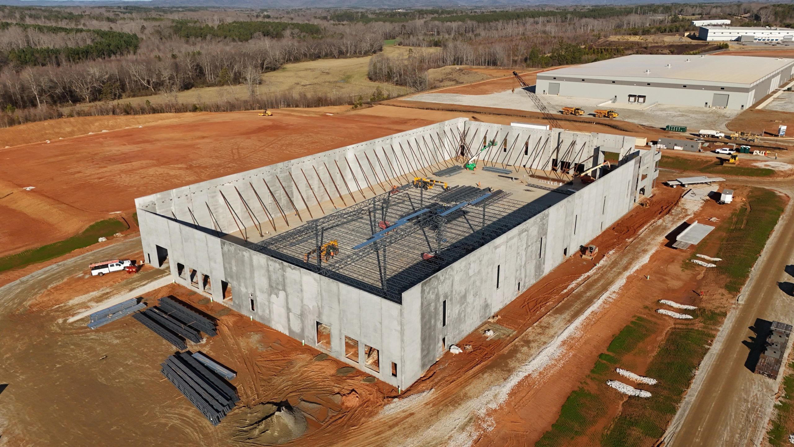 Aerial view of a commercial building under construction with concrete walls and steel roof framing.