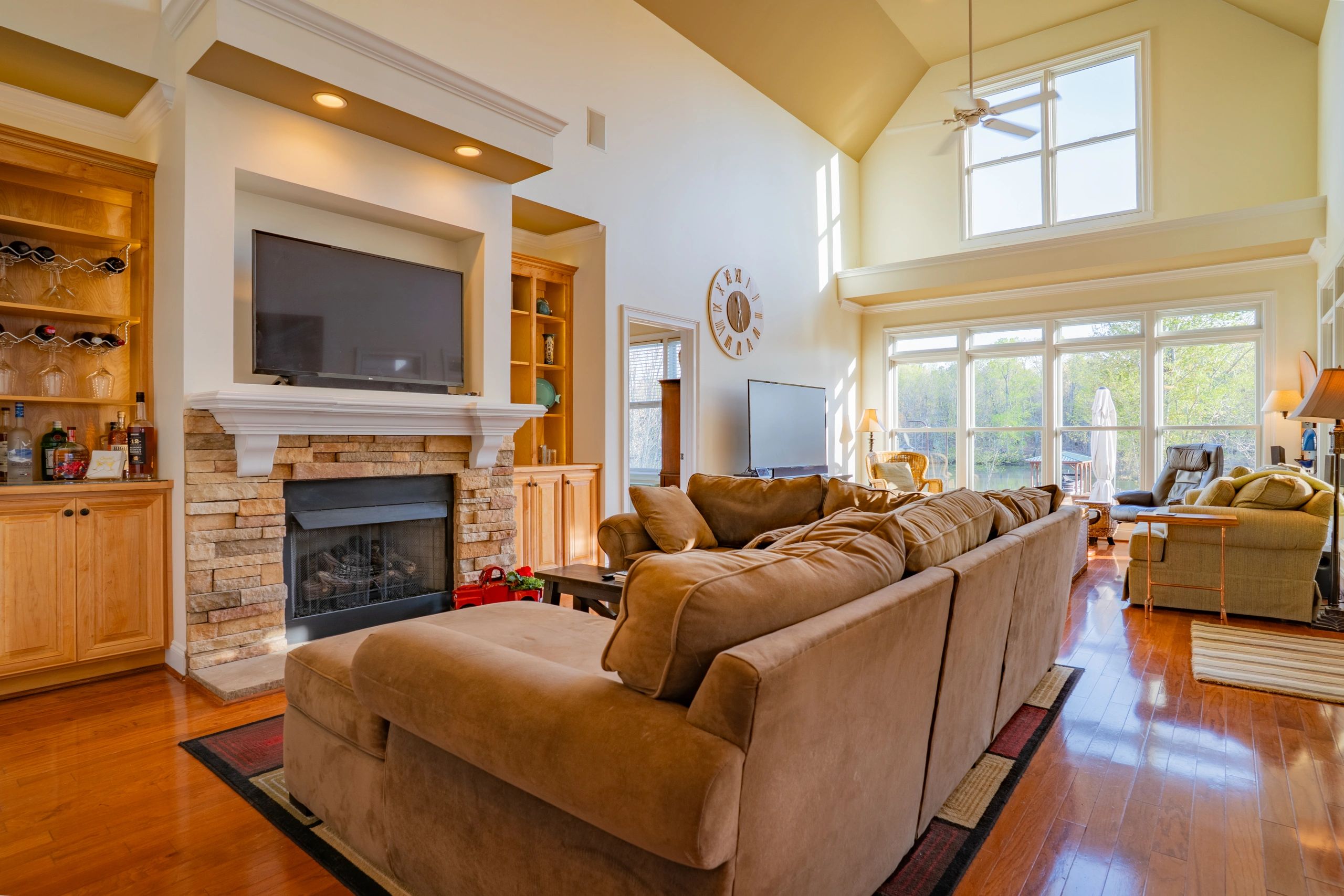Professional interior photograph of a bright living room with a stone fireplace and large windows.