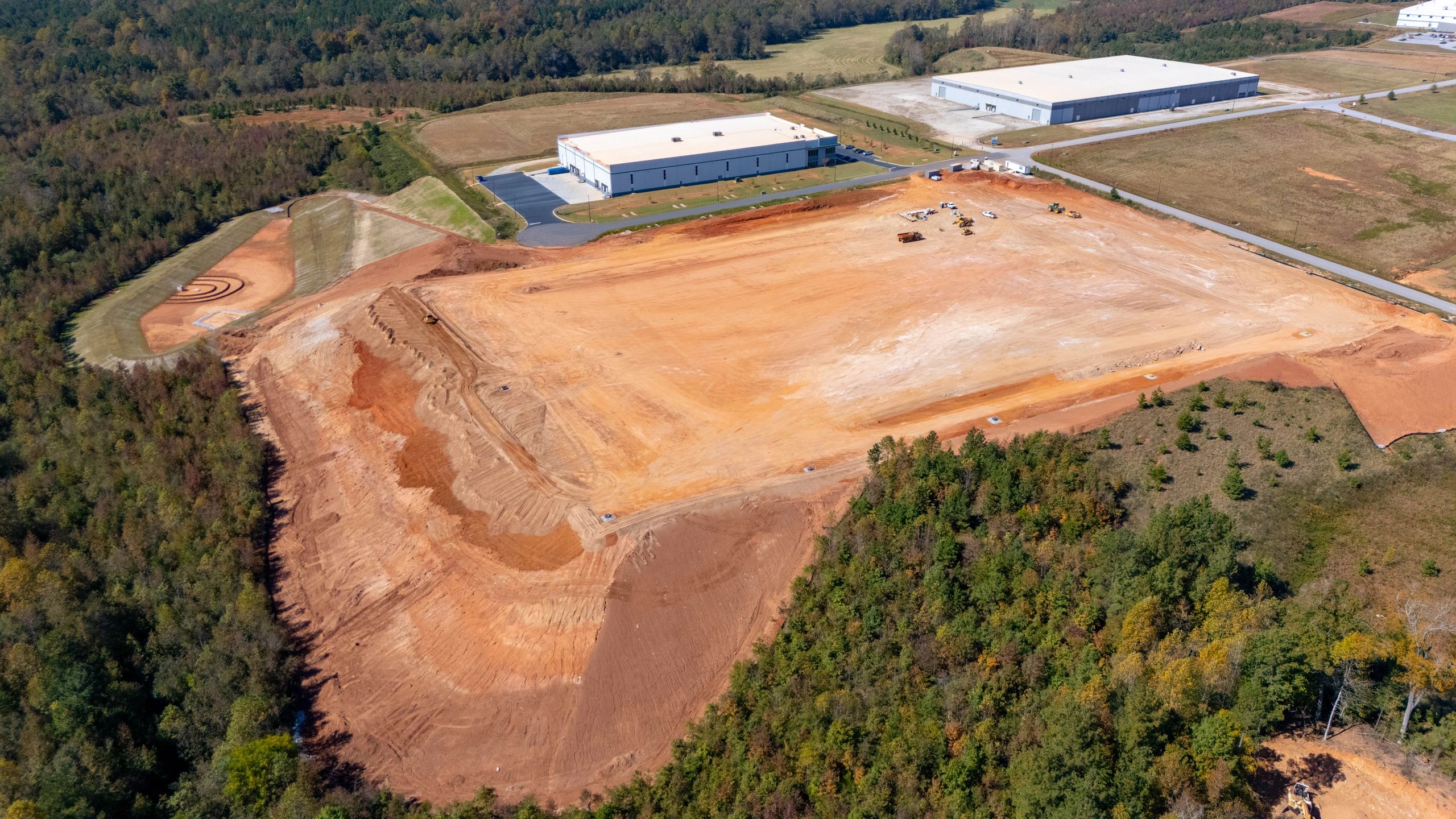 Aerial view of a graded construction pad, nearby buildings, and a stormwater basin.