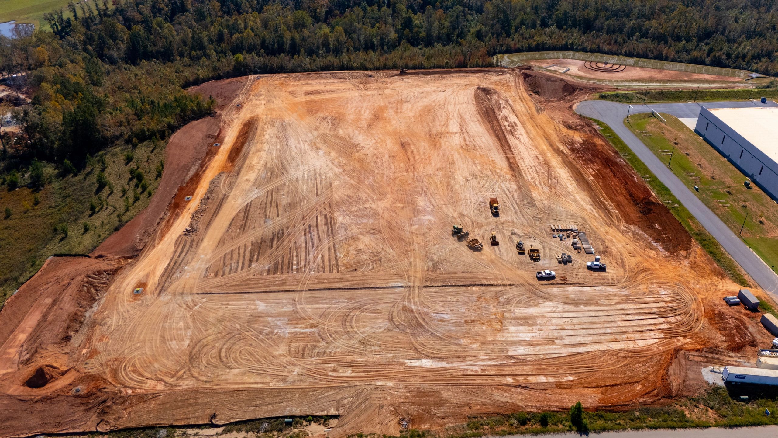 Aerial view of an active graded construction site with equipment and staged drainage materials.